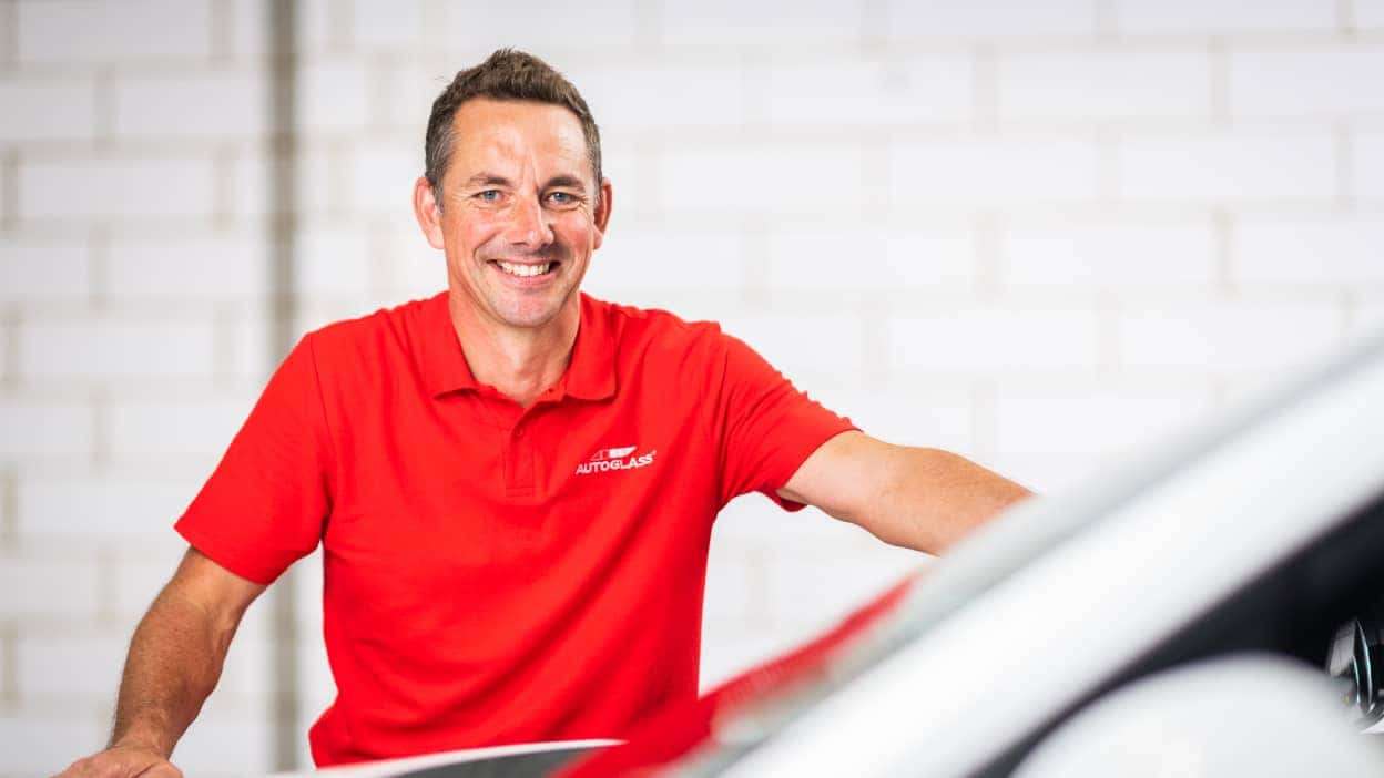 A technician at Autoglass® standing and smiling next to vehicle 